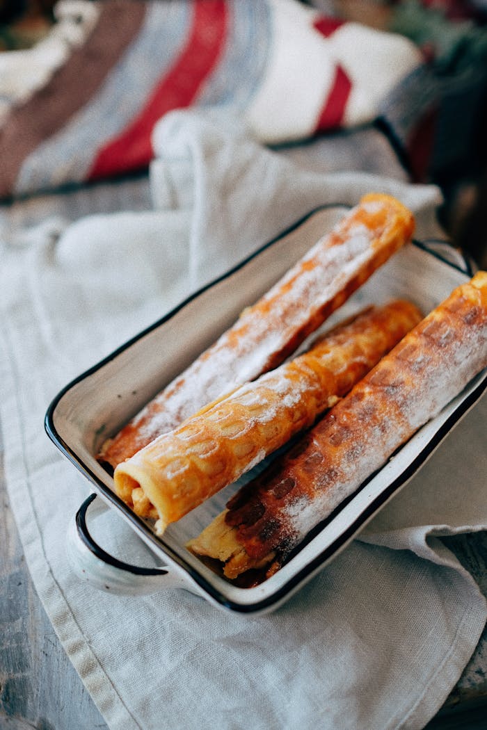 contact-img From above of crispy waffle rolls with sweet filling and powdered sugar in enameled baking dish placed on rustic wooden table